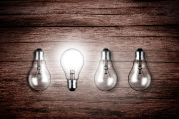 Lightbulbs on wood - A glowing lightbulb contrasts with others as a metaphor for ideas and creativity on problem solving and uniqueness
